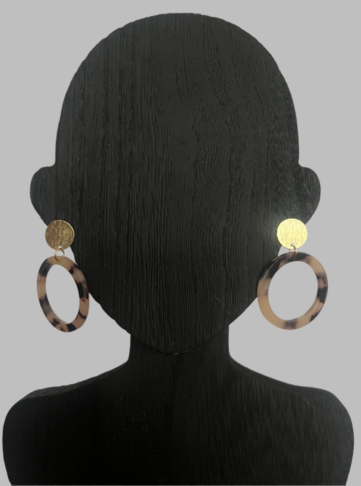 Earrings on a black mannequin head against a plain background