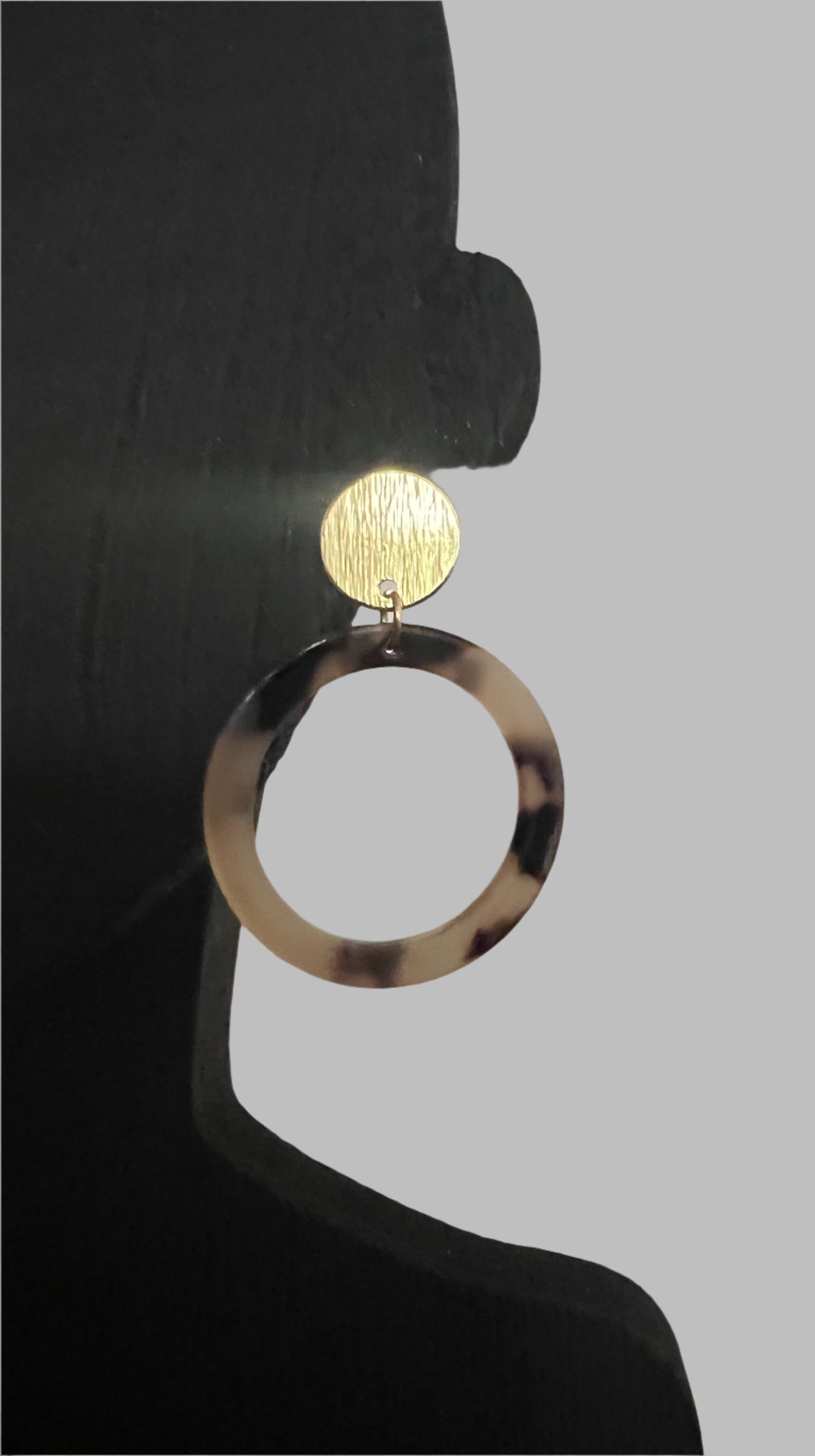 Earring with tortoiseshell hoop and gold circle on a neutral background